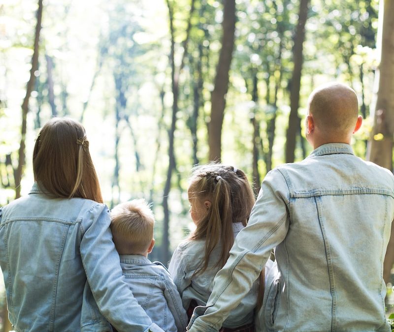 man and woman holding hands together with boy and girl looking at green trees during day